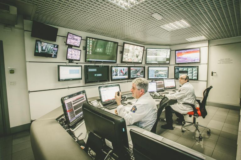 Due operatori monitorano schermi in una sala di controllo.
