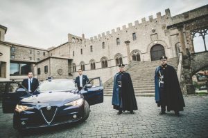Auto blu con uomini in divisa davanti a edificio storico.