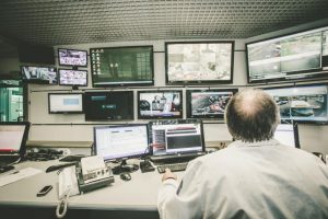 Operatore in sala controllo con molti schermi accesi.
