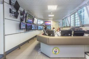 Sala di controllo con monitor e operatori al lavoro.